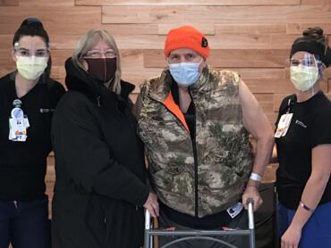 Man wearing a camo vest and orange hunting cap standing with a walker in between a group of women.