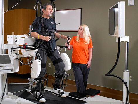 A man harnessed into a robotic body system to practice walking on a treadmill.