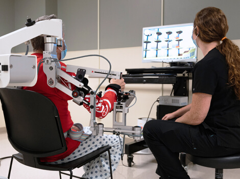 Looking over the shoulder of a patient using a robotic arm trainer to build arm strength.