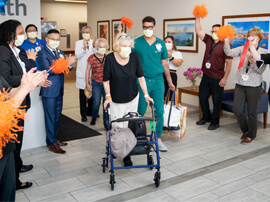 Woman wearing a hospital mask and using a rolling walker to leave the hospital.