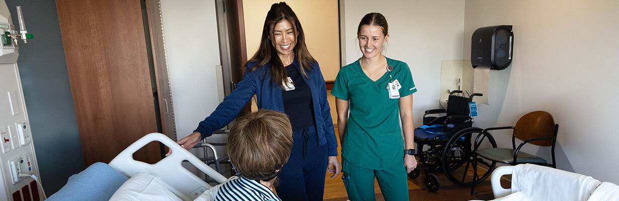 Two nurses smile and discuss progress made with a patient as they sit in their hospital bed.