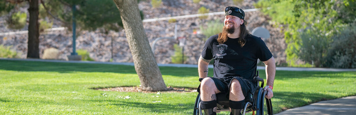 A previous patient smiles as they venture down a path in their wheelchair.