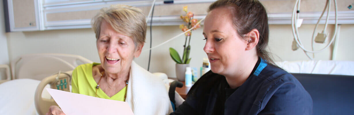 A member of the care team reviews paperwork with a patient at their bedside.