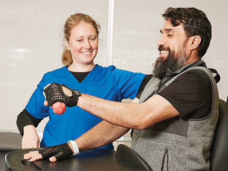 A patient sits and works on arm strength using hand weights with the support of his therapist.
