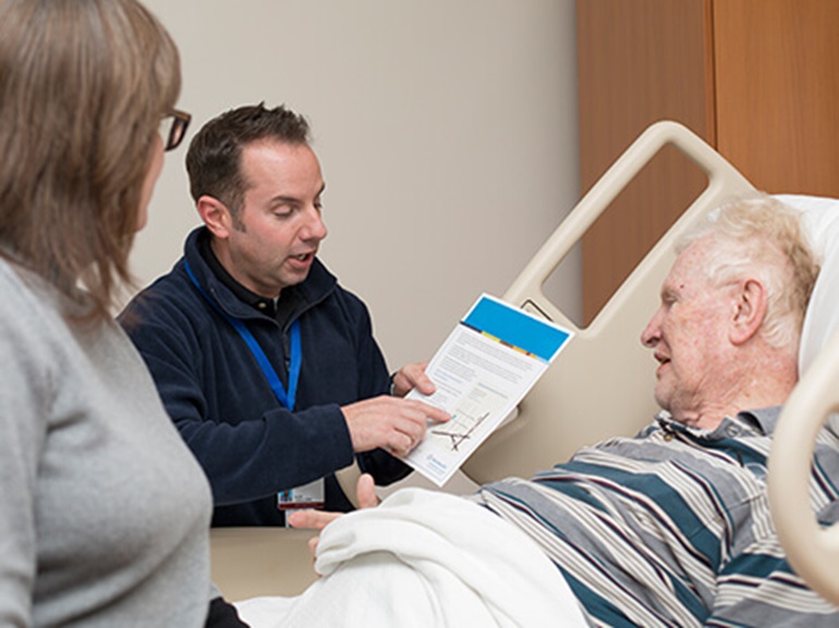 Therapist explaining information to an older man in a hospital bed.