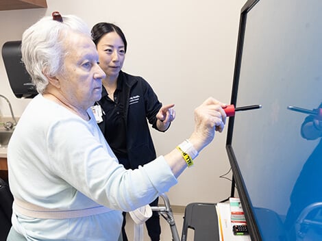 Looking over the shoulder of a patient using a robotic arm trainer to build arm strength.