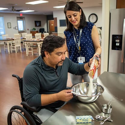Patient in a wheelchair is pouring food into a bowl with the support of his occupational therapist