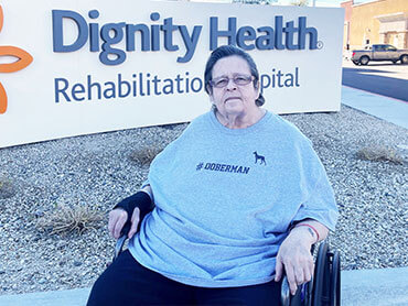 A woman with short dark hair sitting in a wheelchair outside Dignity Health Rehabilitation Hospital.